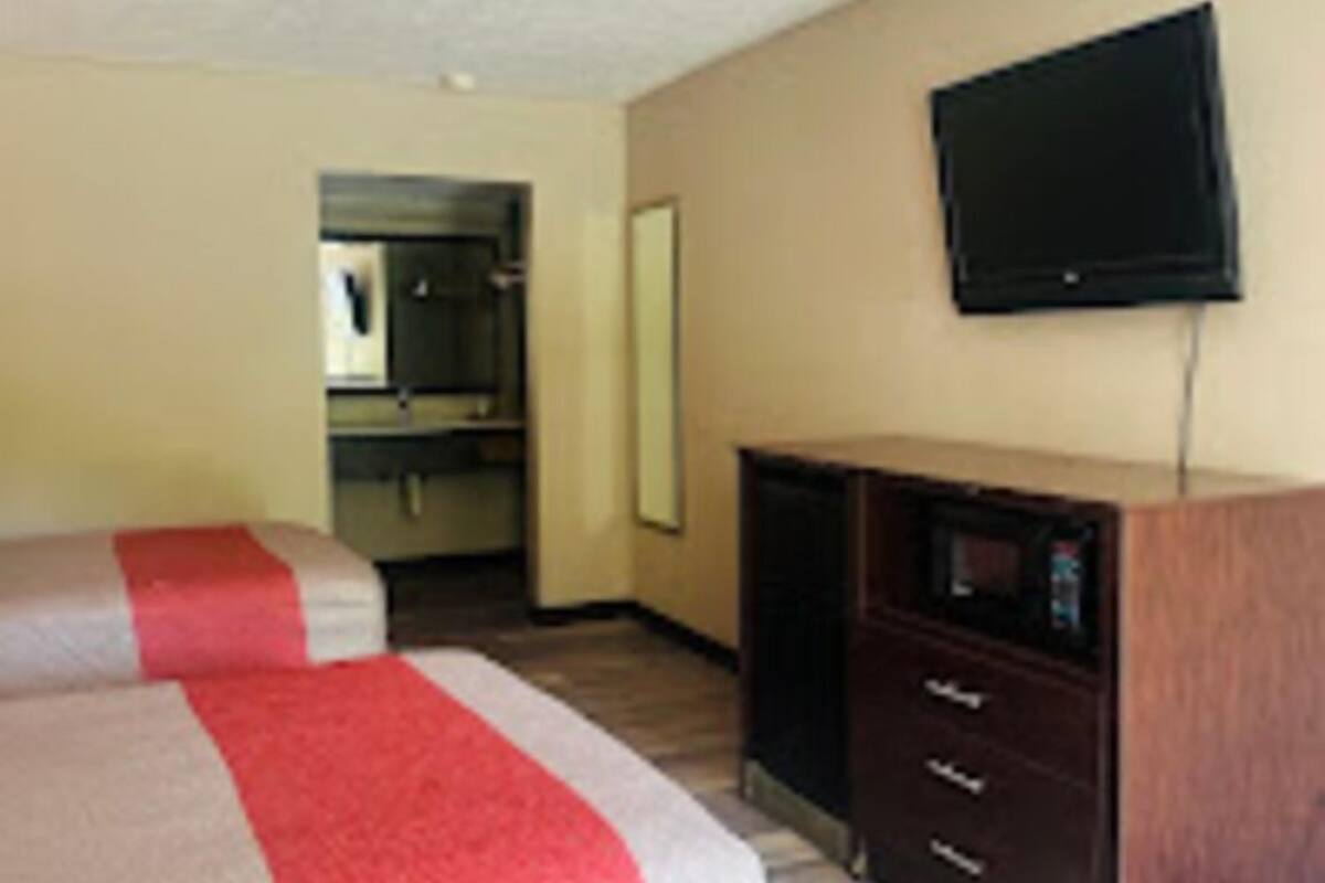 Una habitación de hotel con dos camas, un televisor de pantalla plana, un aparador y un microondas.