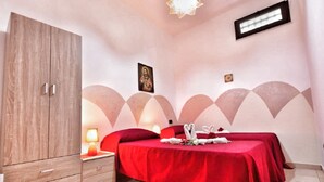 Ein Schlafzimmer mit einem Holzschrank, einem Bett mit roter Bettdecke, einem Nachttisch mit Lampe und einer Wand mit dekorativem Muster.