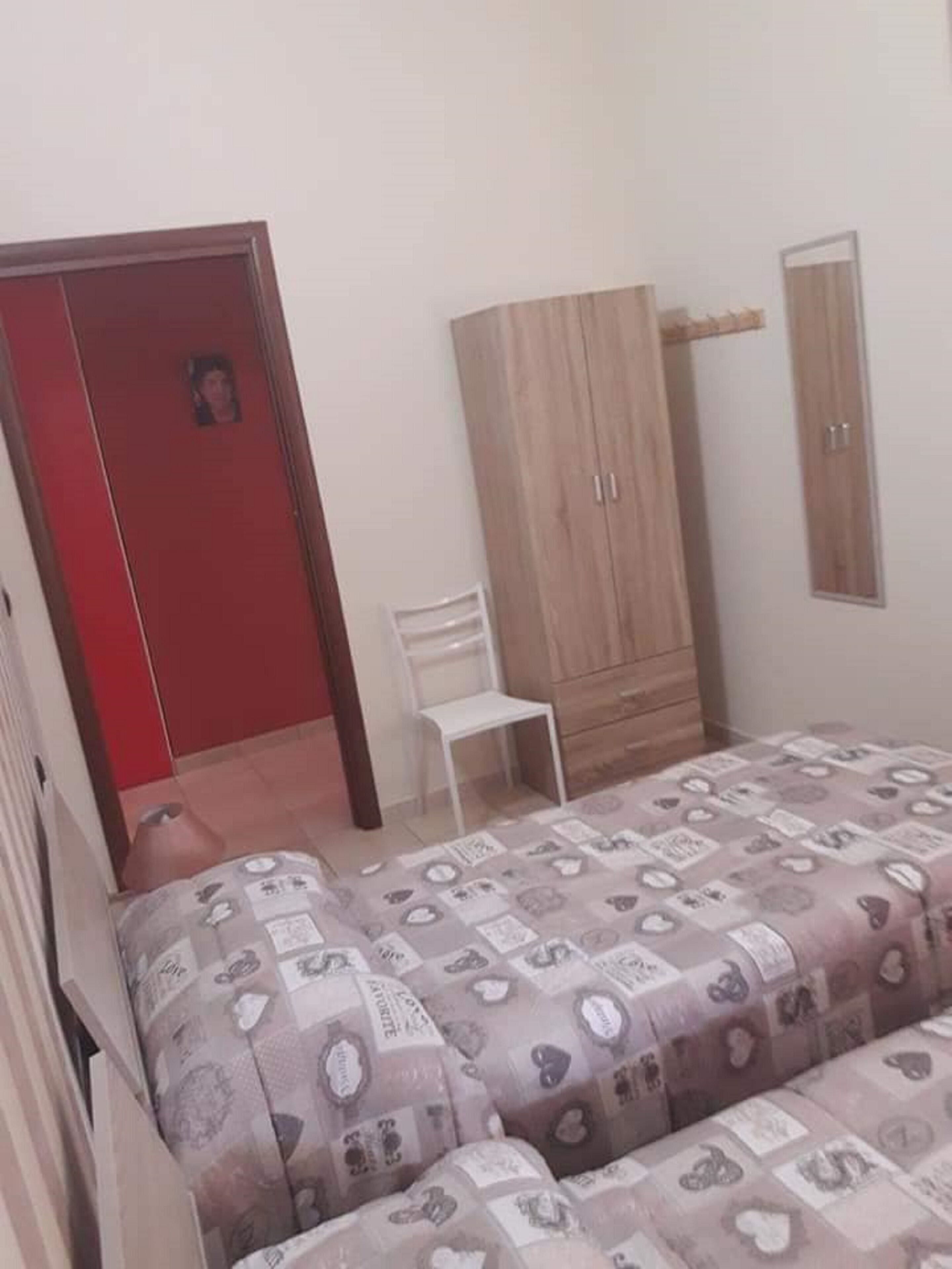 A bedroom with a bed, a wardrobe, a chair, and a mirror.