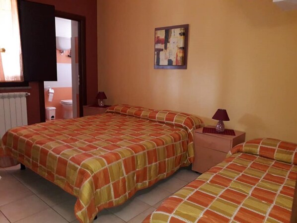 A bedroom with two beds, a nightstand, a lamp, and a painting on the wall. - B&b Santa Sofia by holidayngo (Mileto)