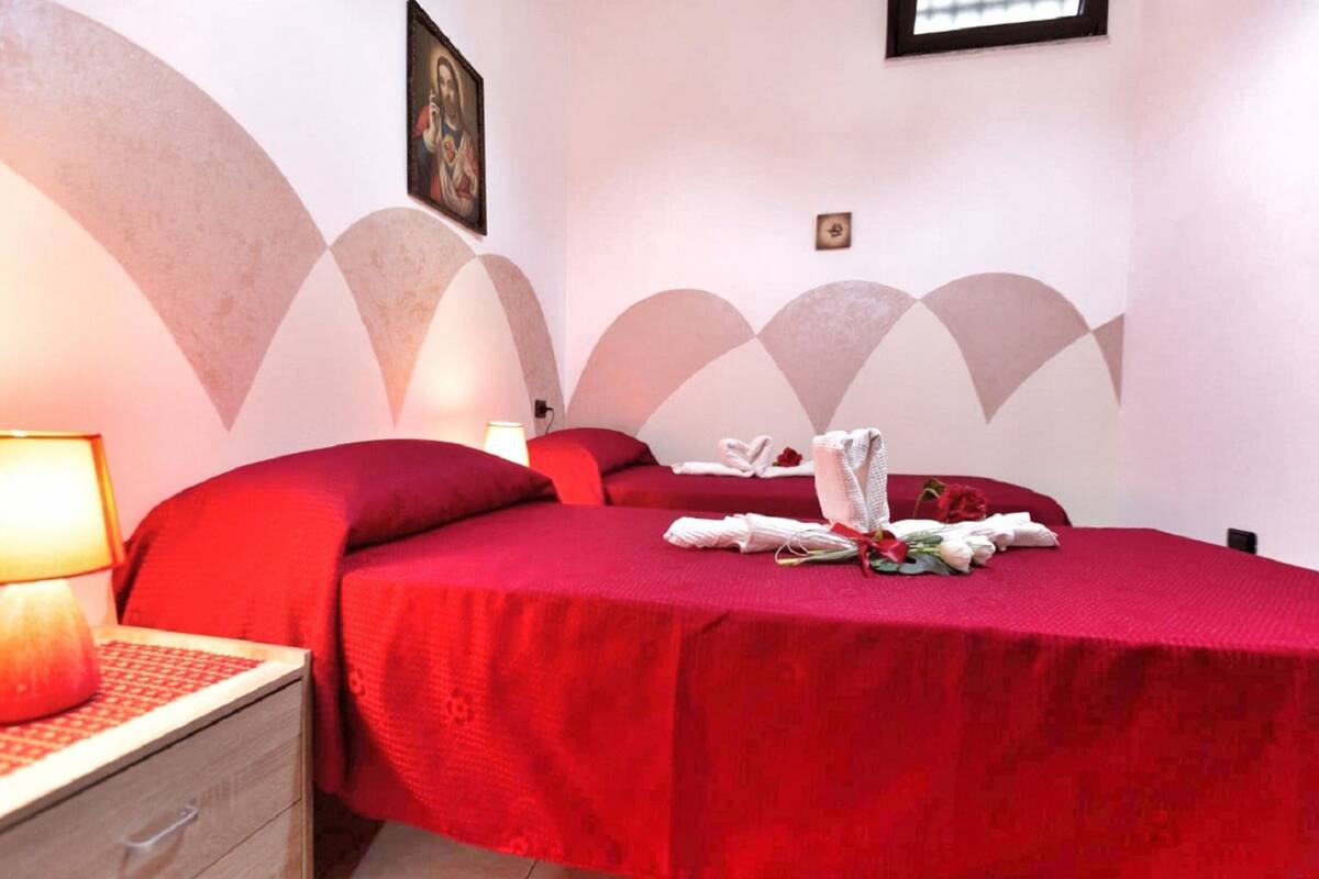 Ein Hotelzimmer mit roter Bettdecke, einer Nachttischlampe und einem Blumenstrauß auf dem Bett.