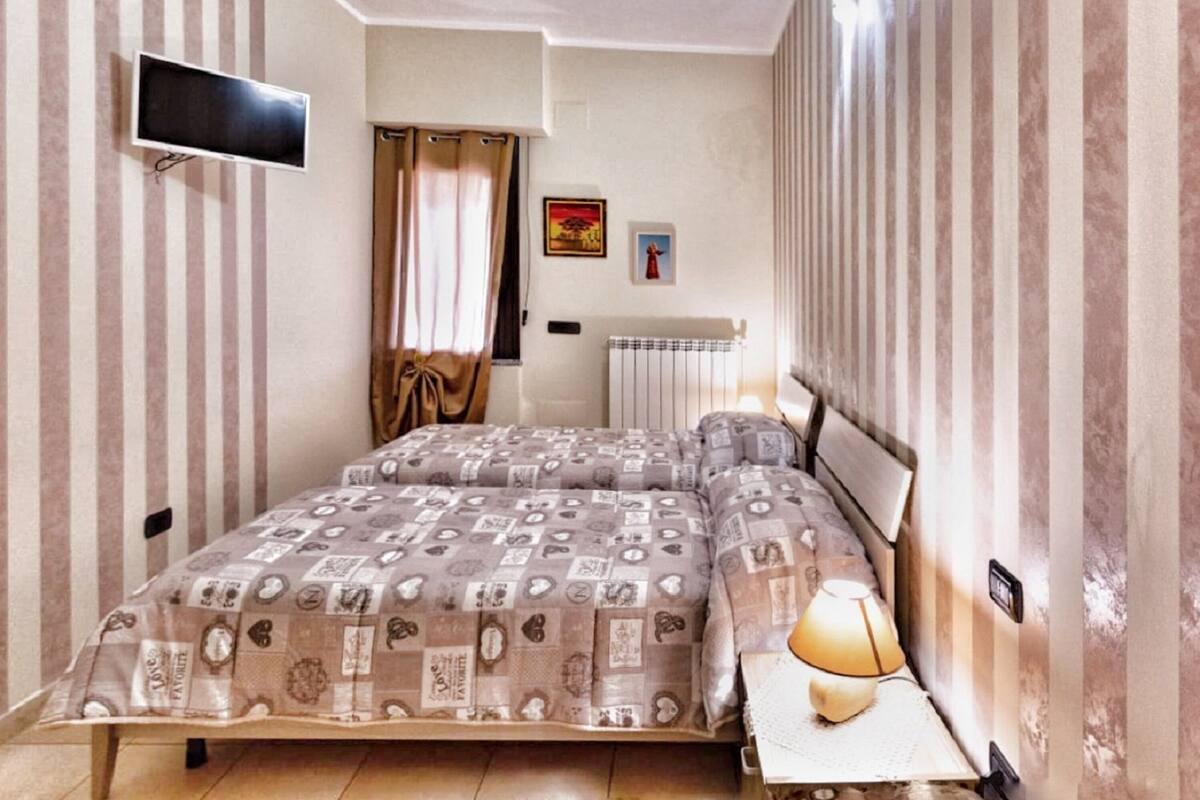 Ein Schlafzimmer mit einem Bett, einer Nachttischlampe, einem an der Wand montierten Fernseher und einer Heizung.