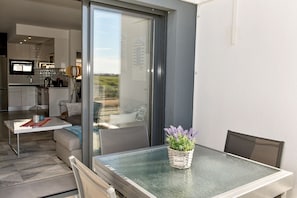 A modern kitchen with a large window, a dining area with a glass table, and a balcony with a view.