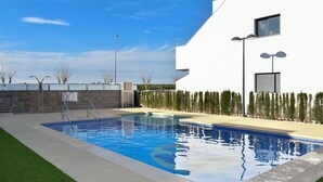 Een modern buitenzwembad met een helderblauw wateroppervlak, omgeven door een verzorgd gazon en een wit gebouw met een plat dak.