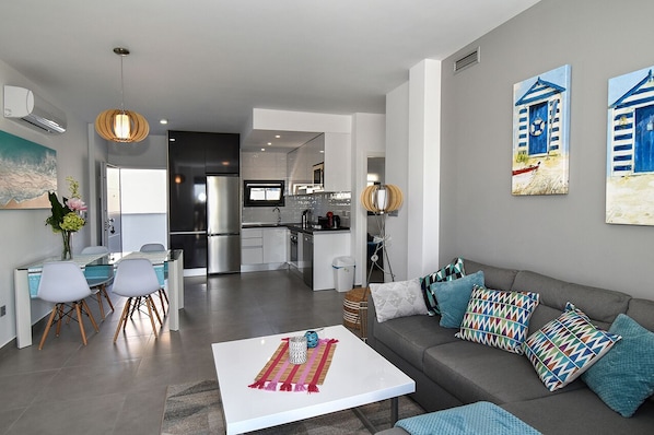 A modern living room with a grey sofa, a white coffee table, and a dining area with a glass table and chairs.