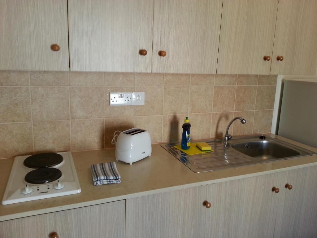 A small kitchenette with a stove, toaster, sink, and cabinets.
