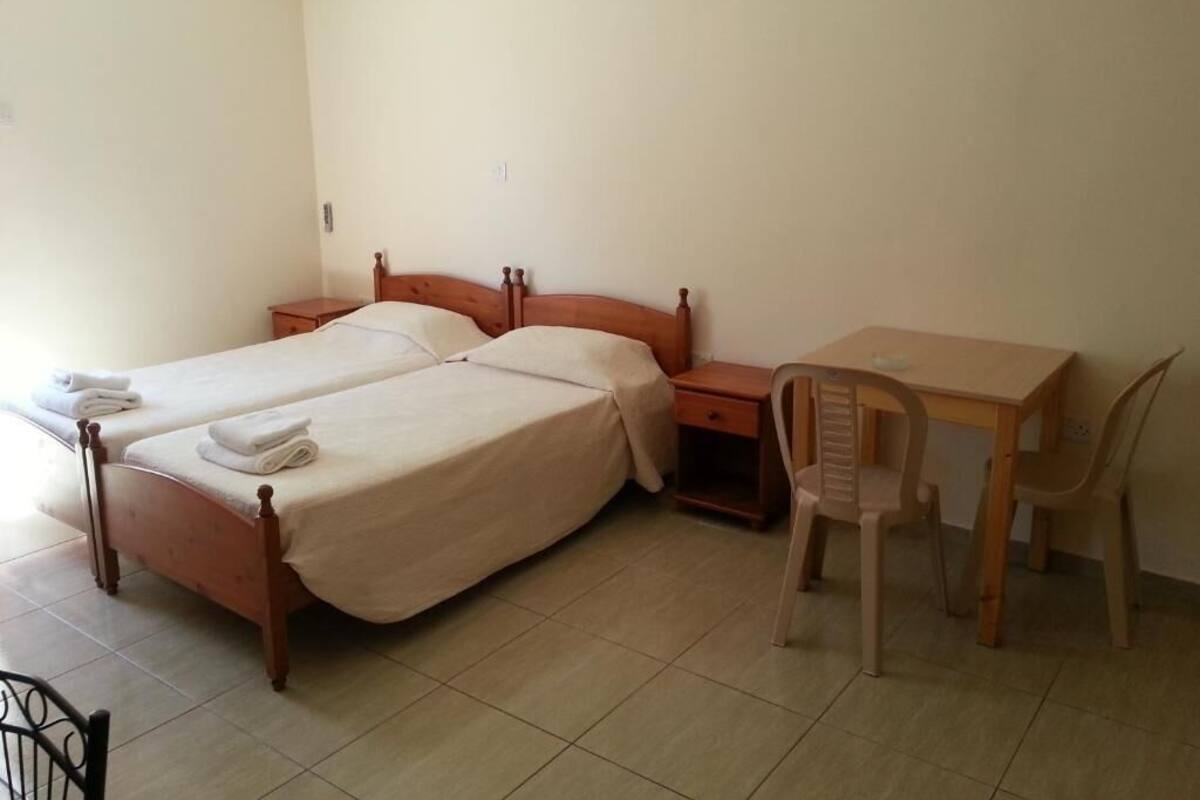 Una habitación con dos camas individuales, un escritorio de madera, una silla y una mesita de noche pequeña.