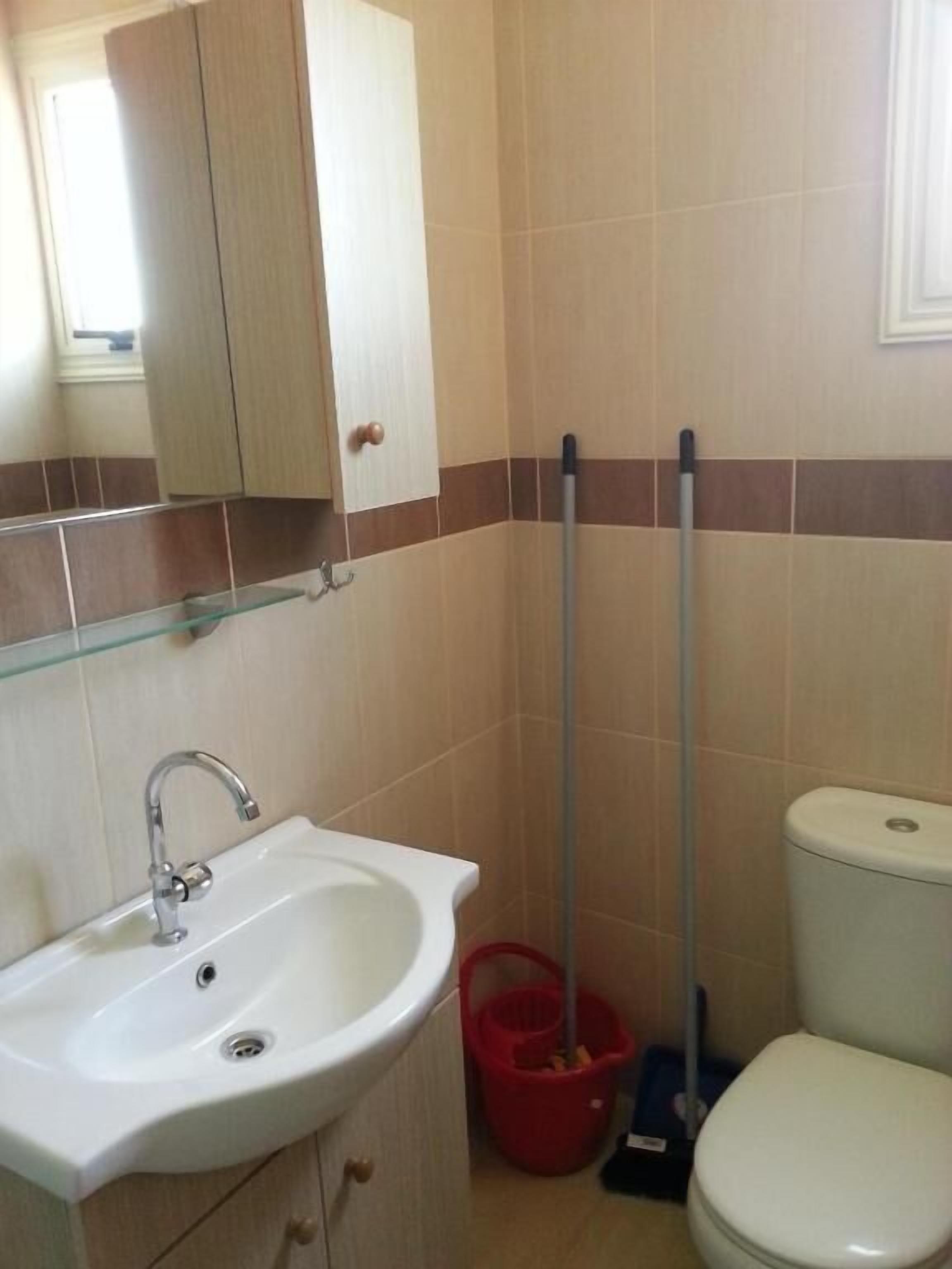 Ein Badezimmer mit weißem Waschbecken, einem Spiegel, einer Toilette und einem an die Wand gelehnten Mopp.