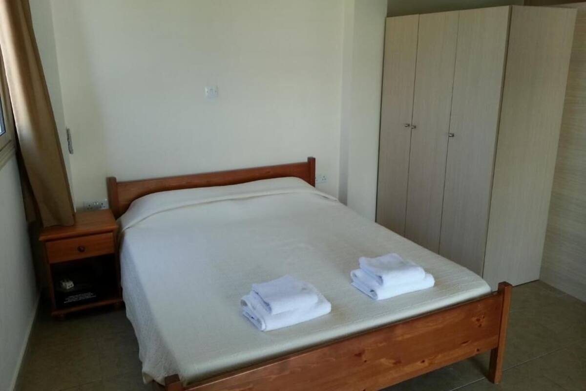Una cama individual con estructura de madera, una mesita de noche, un armario y una cortina.