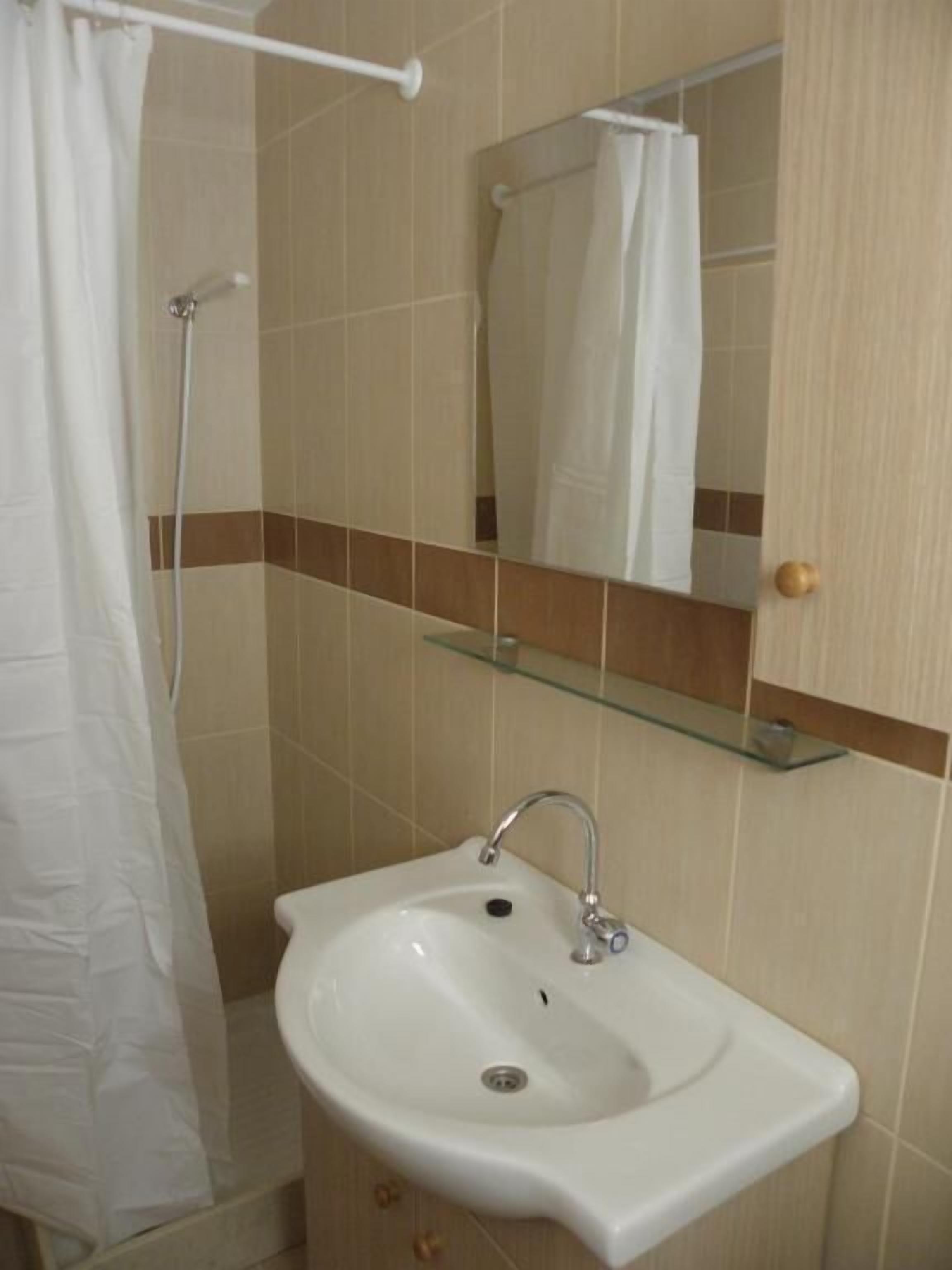 A bathroom with a white sink, a glass shelf above it, and a shower curtain.