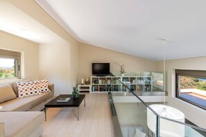 A modern living room with a sofa, coffee table, TV, bookshelf, and a balcony with a glass railing.