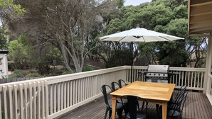 En træterrasse med et bord, stole, en parasol og en grill.