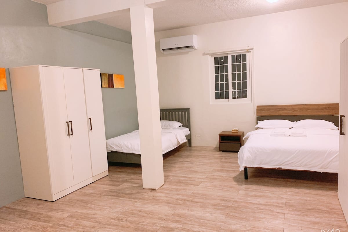 A room with two beds, a wardrobe, a window, and an air conditioning unit.