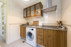 A compact kitchen with a built-in washer, wooden cabinets, and a countertop with various appliances.