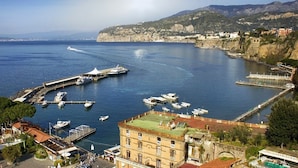 A coastal town with a marina, buildings with red-tiled roofs, and a clear view of the sea and distant mountains. - Al Campanile (Sant'Agnello)