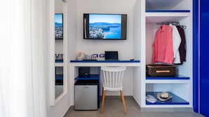 A modern room with a desk, a chair, a television, a mini-fridge, and a wardrobe with hanging clothes and a suitcase. - Al Campanile (Sant'Agnello)
