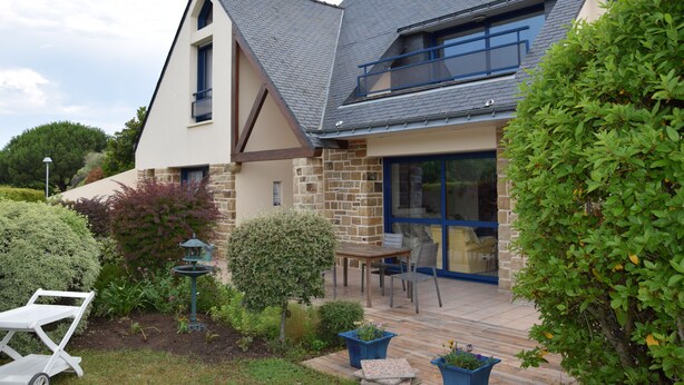 Una casa moderna con techo inclinado, fachada de piedra y un patio con mobiliario exterior.