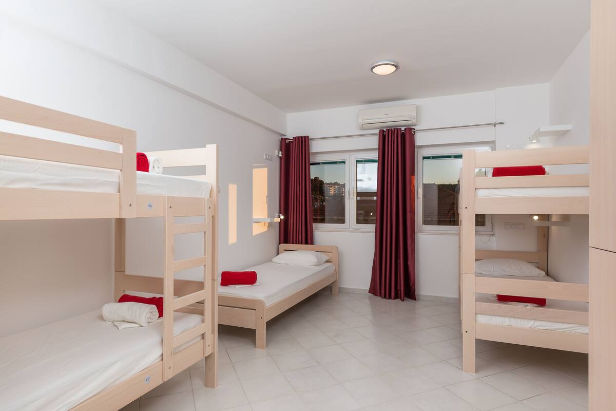 A room with bunk beds, a single bed, and a window with curtains.