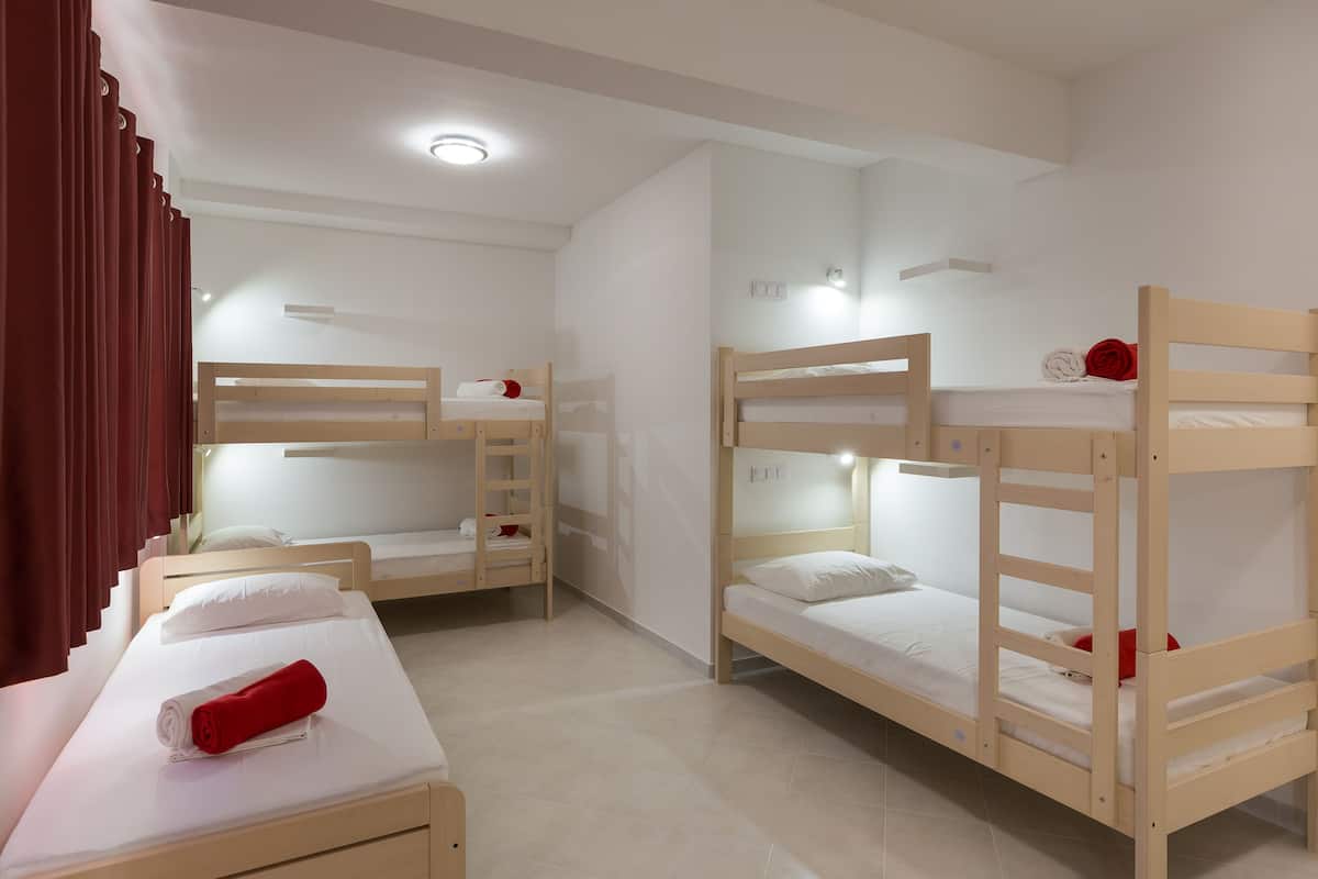 A room with three bunk beds, each with a wooden frame and white bedding. There is a red towel on the bed in the foreground.