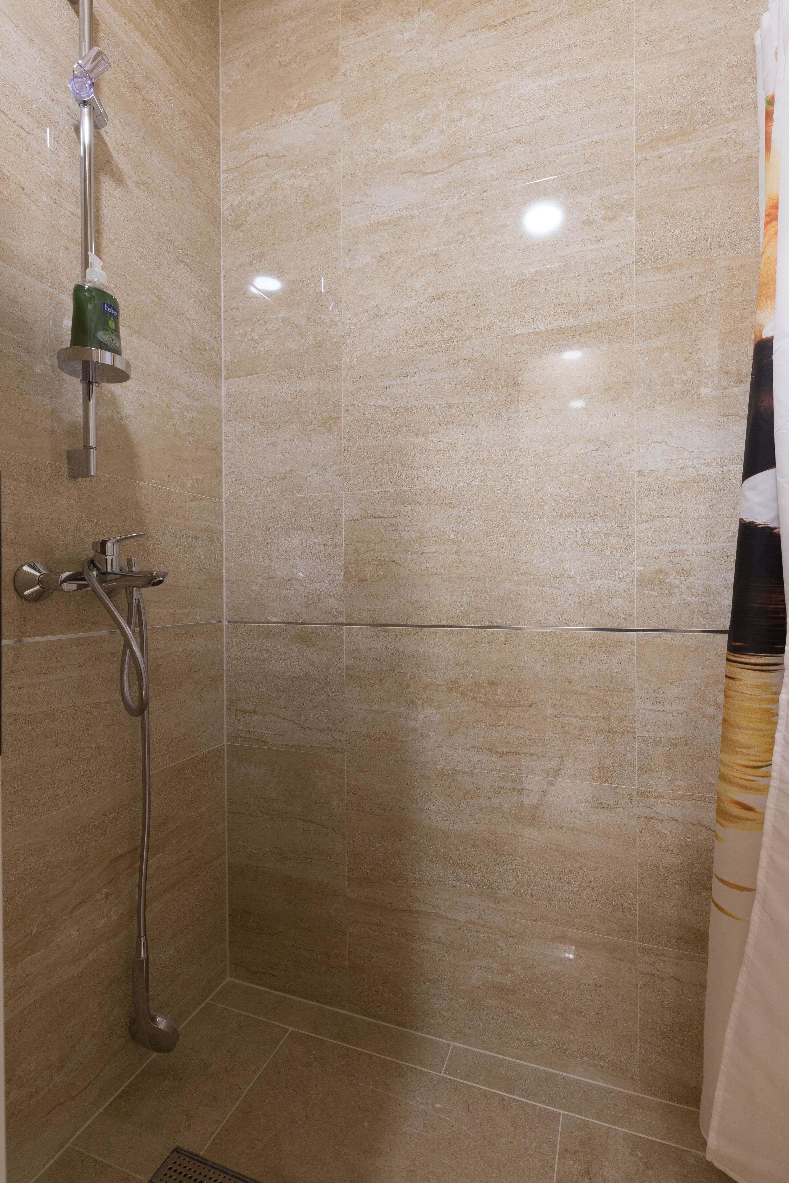 A bathroom with beige tiles, a shower with a handheld showerhead, and a toilet.