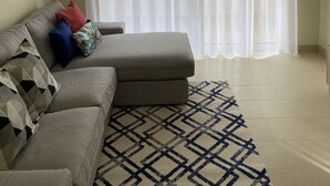 Una sala de estar con un sofá, un tapete estampado y cortinas traslúcidas.
