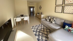 Una sala de estar con sofá, televisión, mesa de comedor con sillas y alfombra estampada.