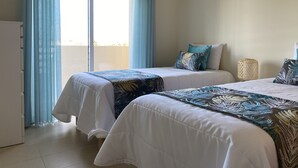 Habitación de hotel con dos camas, vista al mar a través de amplios ventanales y un balcón.