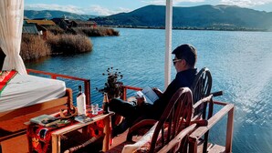 A person reading on a deck with a view of a lake and mountains.