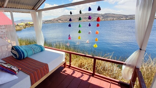 A cozy balcony with a bed, a view of a lake, and colorful hanging decorations.