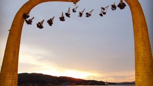 A heart-shaped arch with hanging birds, a wooden bench, and a view of the sunset over water.