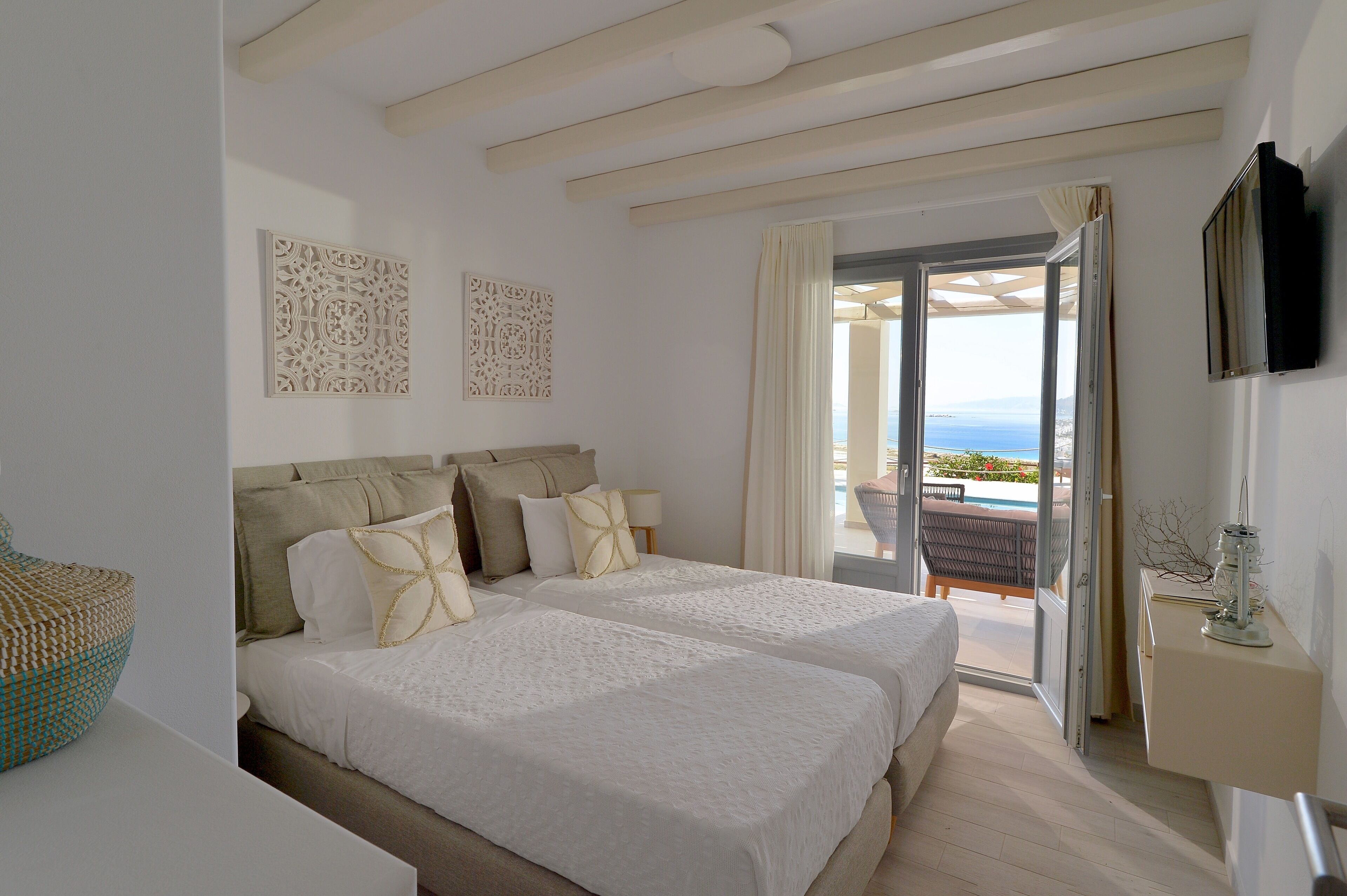 A hotel room with two beds, a balcony with a pool view, and a TV mounted on the wall.