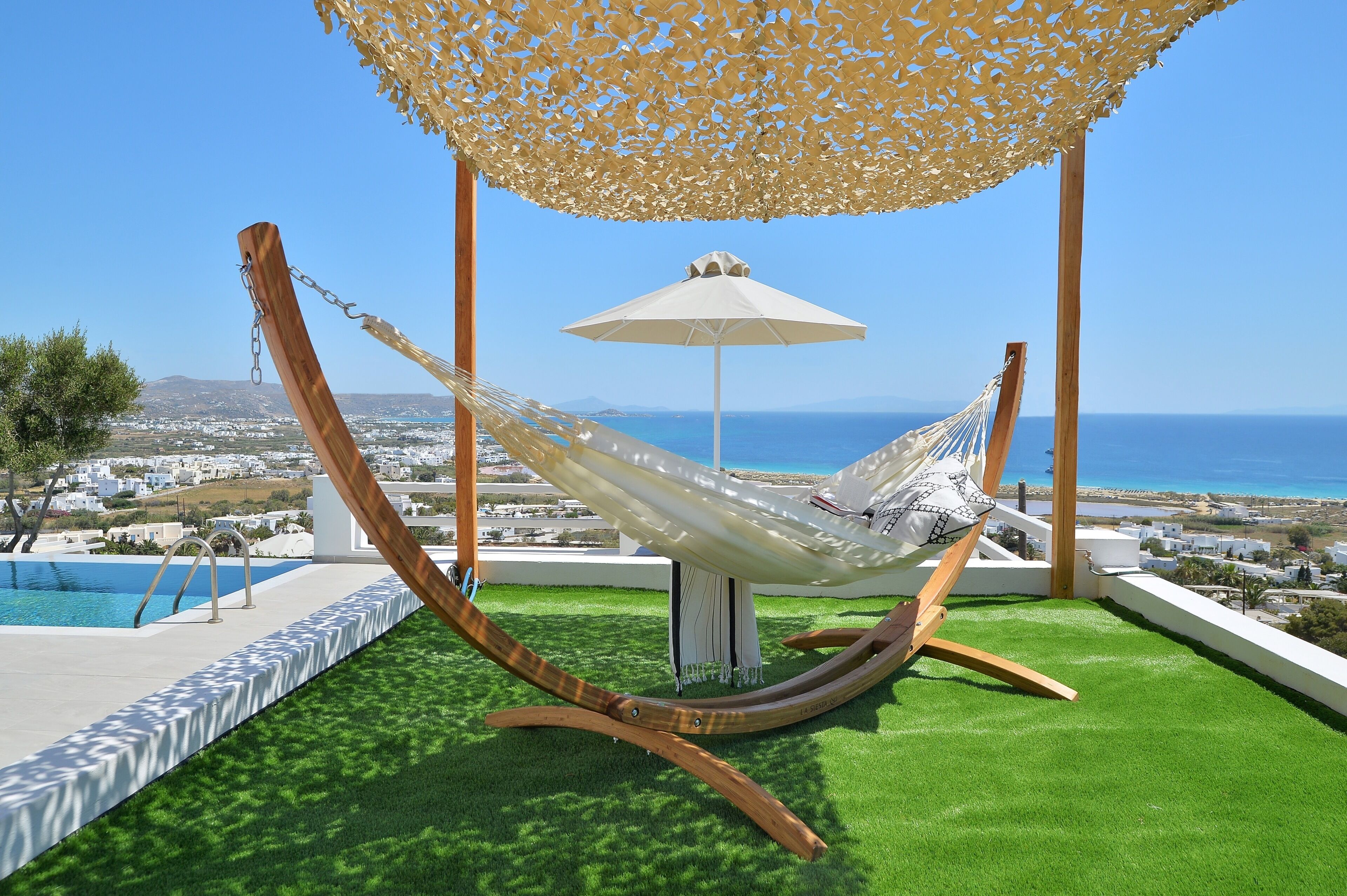 A hammock under a canopy on a rooftop with a pool and a view of the sea.