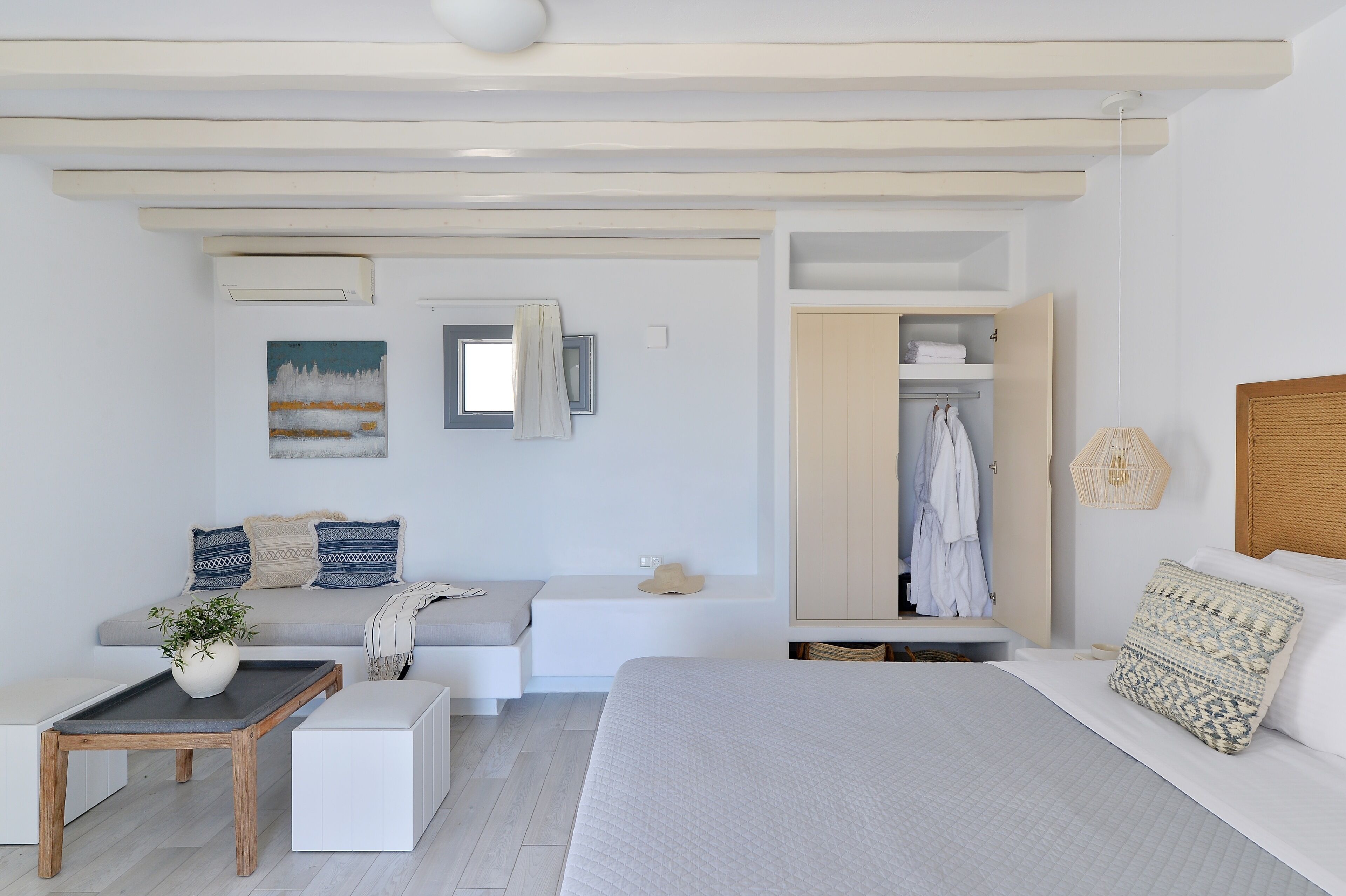A modern bedroom with a bed, a seating area with a bench, a small table with a plant, and a wardrobe.