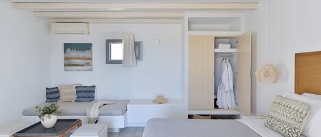 A modern bedroom with a bed, a seating area with a bench, a small table with a plant, and a wardrobe.