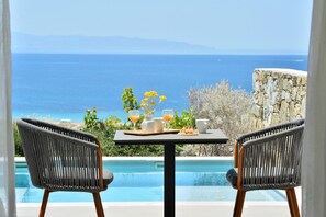 Une table à manger avec vue sur l’océan, deux chaises en osier et un mur en pierre.