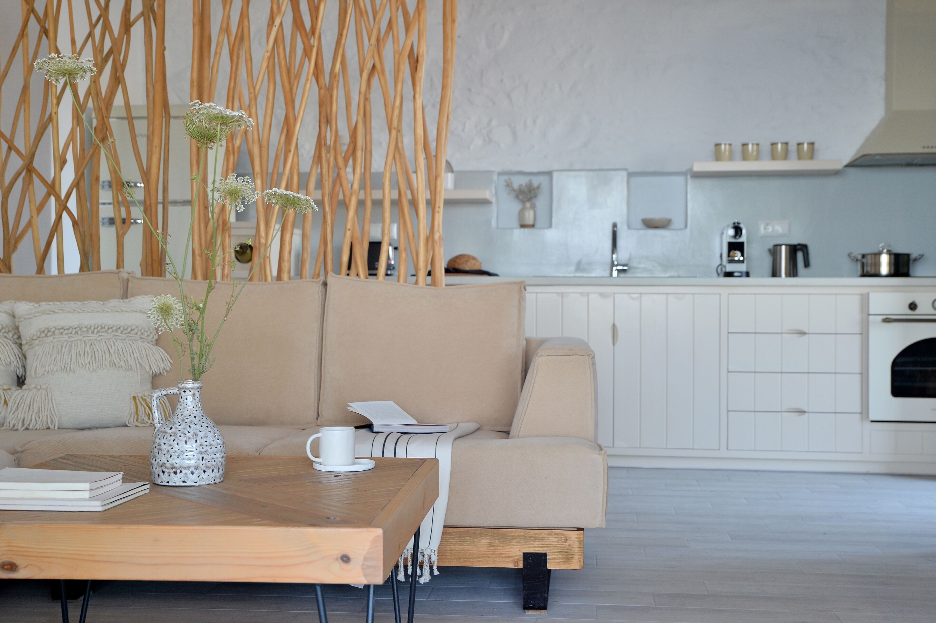 Un salon moderne avec un canapé beige, une table basse en bois et un coin cuisine à l’arrière-plan.