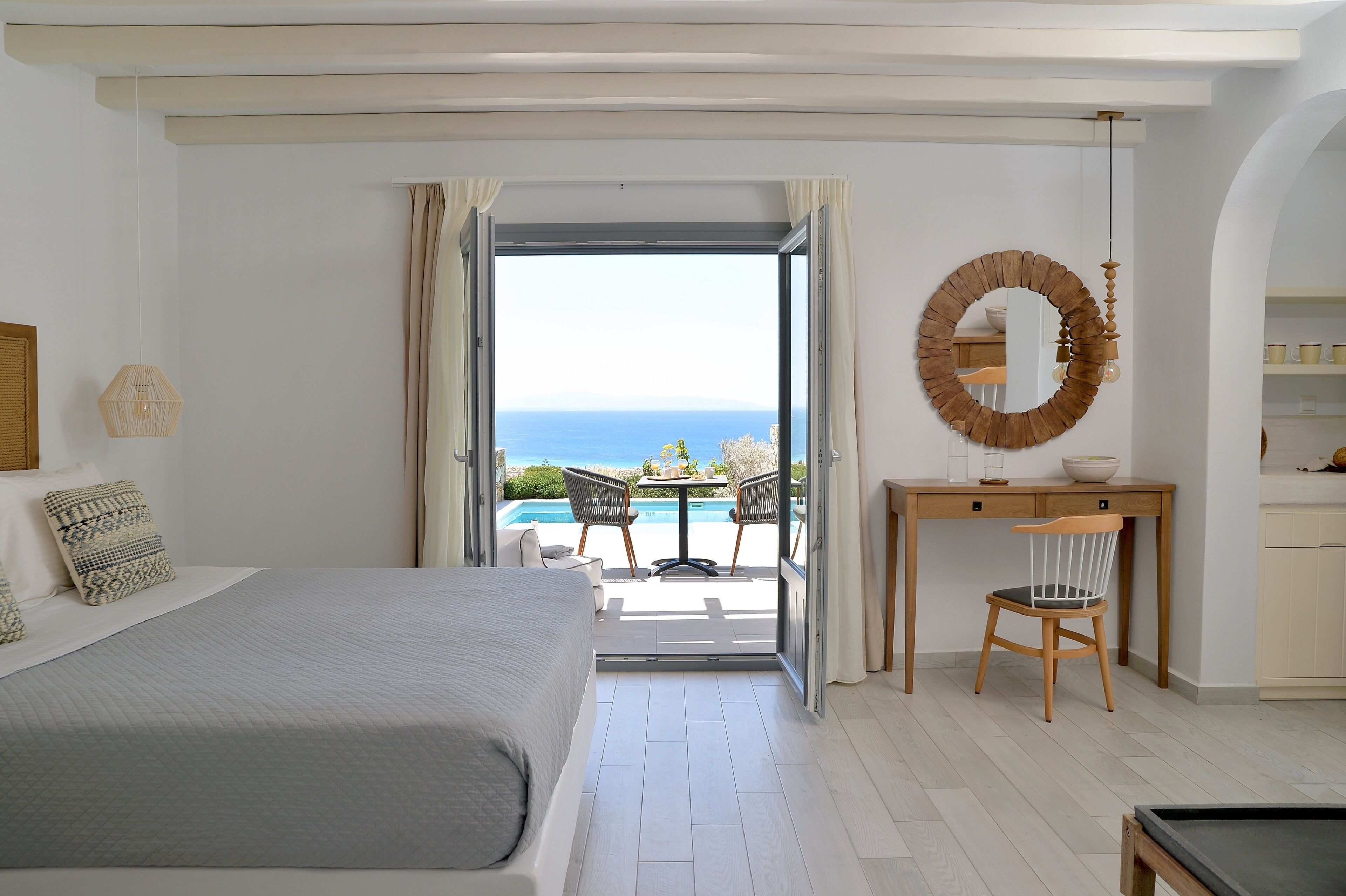 A bedroom with a bed, a desk, a chair, and a view of the sea.