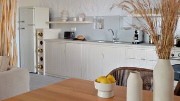 A modern kitchen with white cabinetry, a wooden dining table with a bowl of fruit, and a vase with dried plants.