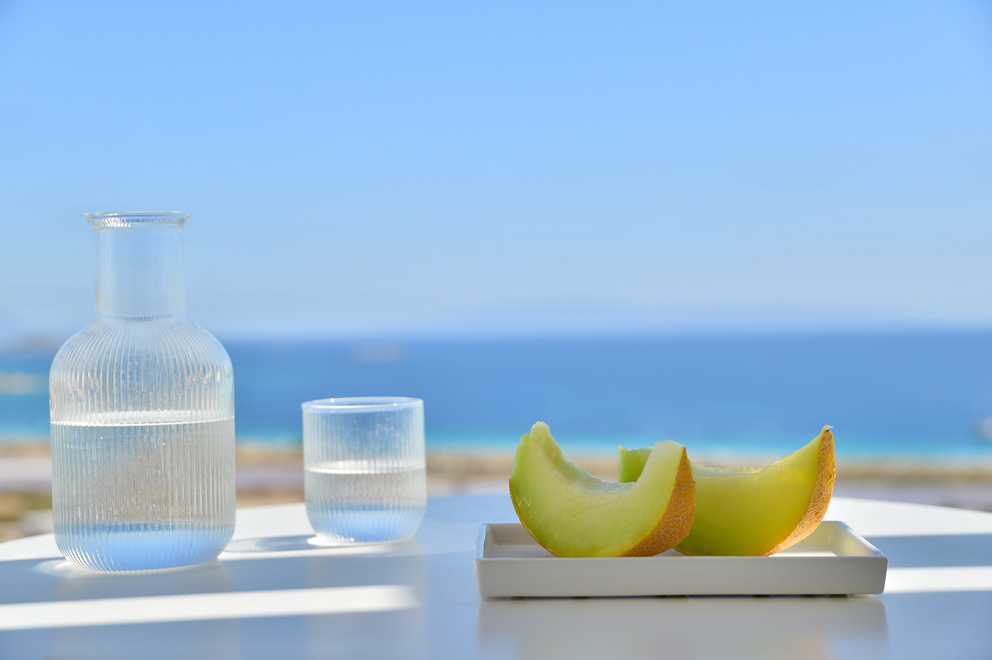 A table with a glass bottle and a glass of water, and a plate with melon slices.