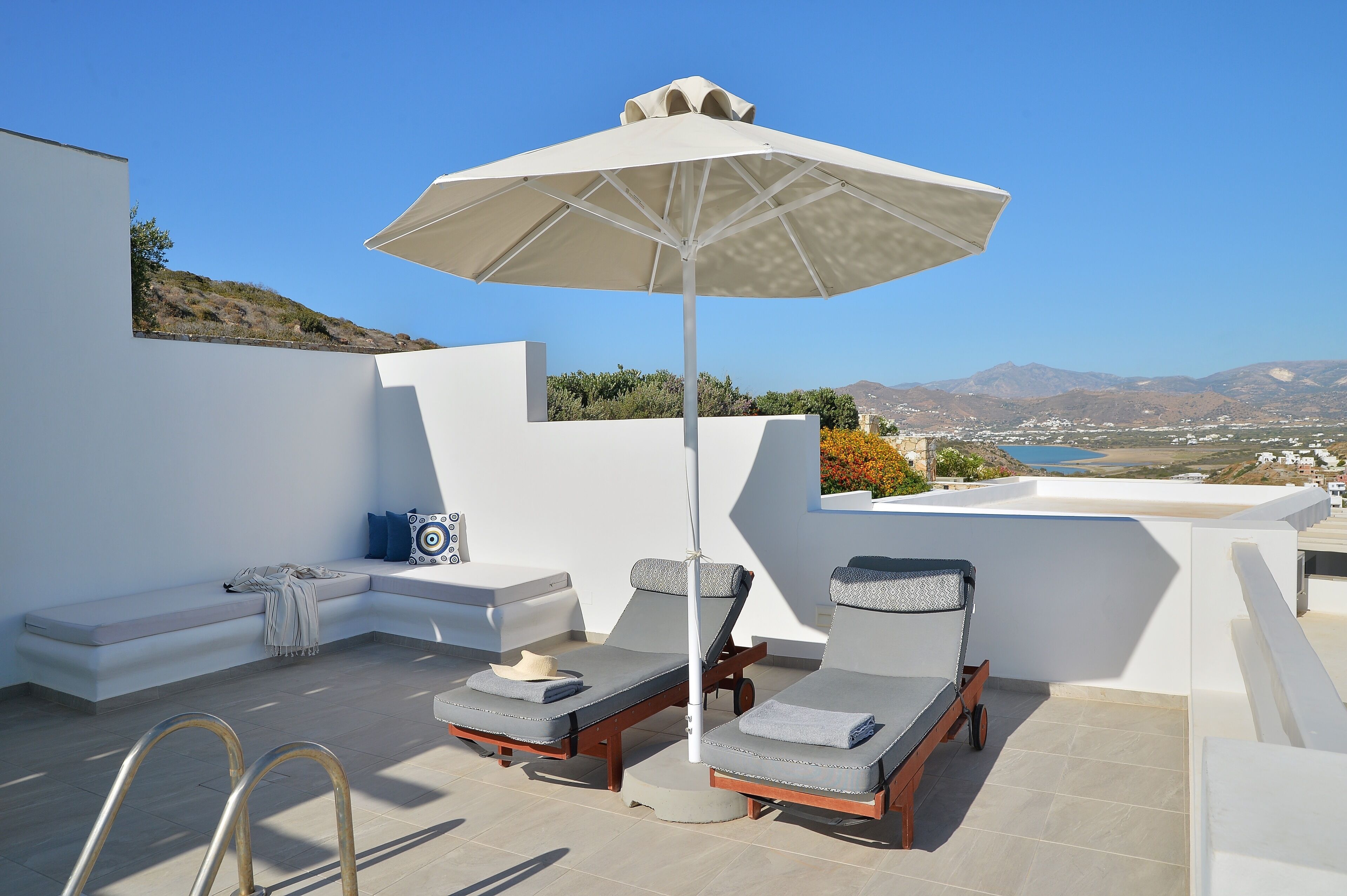 A rooftop terrace with two lounge chairs, a large umbrella, and a view of the landscape.