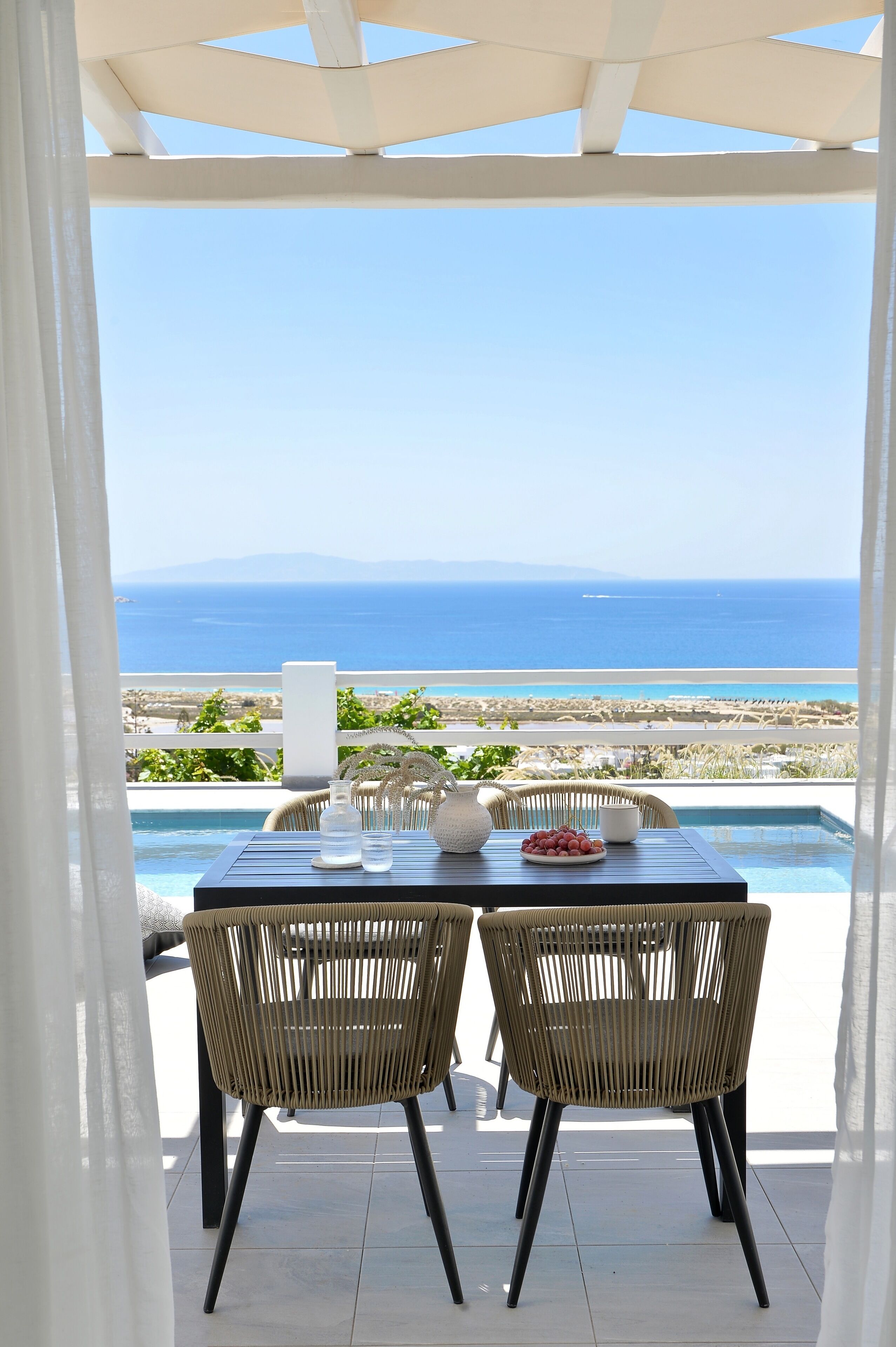 Una terraza con mesa y sillas que da a una piscina y al mar.