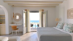 A bedroom with a large bed, a desk, and a chair, with a view of the beach through open doors. - Mythology Naxos Villas & Suites (Naxos)