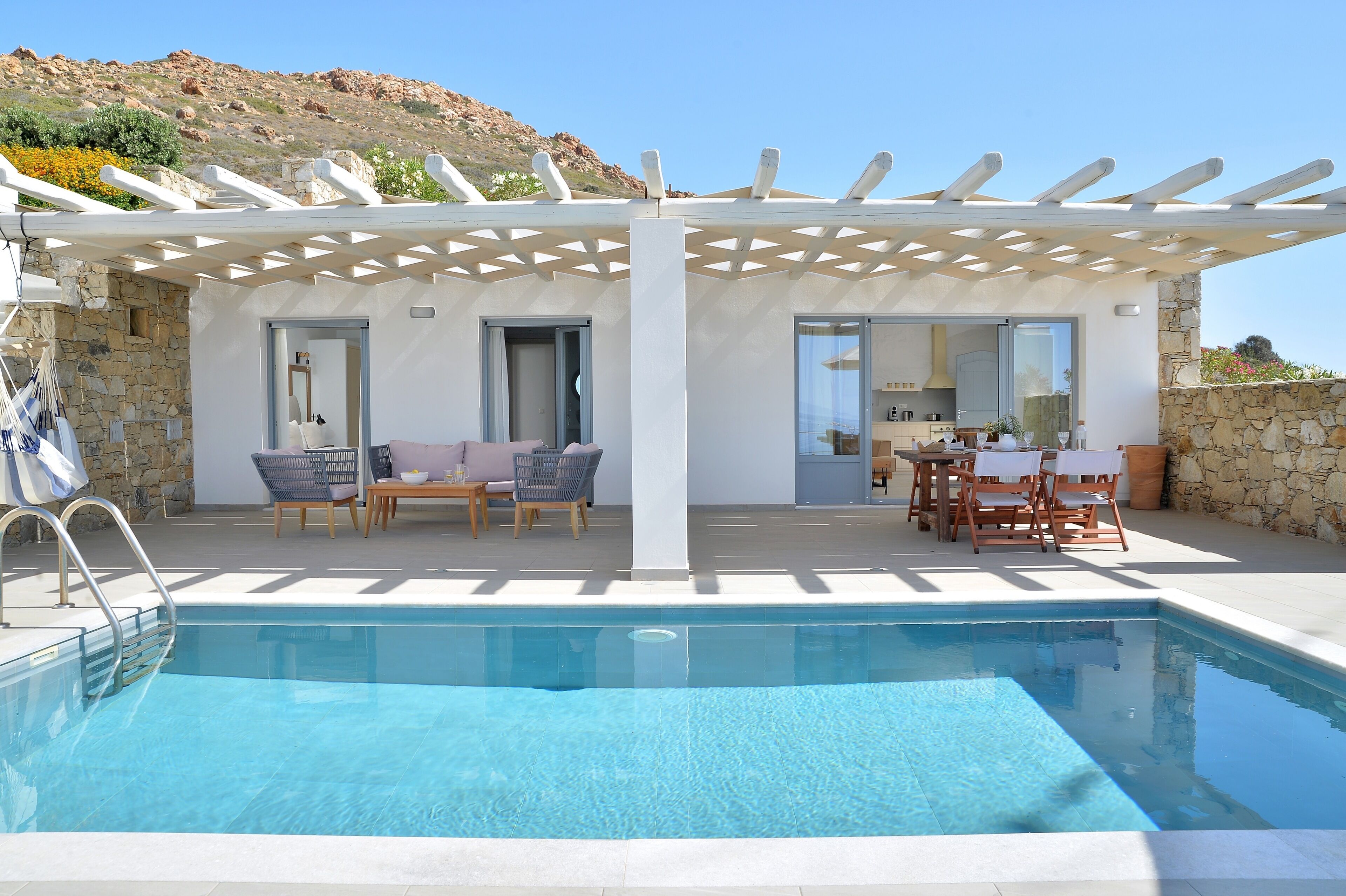 Un área de piscina con pérgola, paredes de piedra y mobiliario exterior.