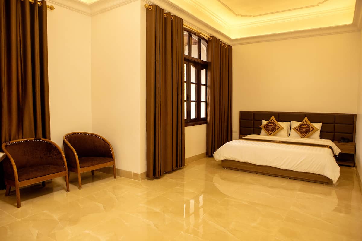 A hotel room with a bed, two armchairs, a window with curtains, and a nightstand.