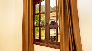 A window with brown curtains, a view of a building with a tiled roof, and a landscape with trees. - Van Xuan Royal Hotel (Ninh Binh)