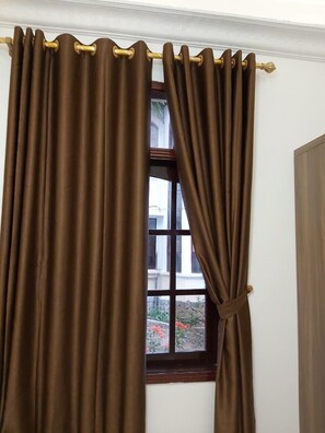A window with brown curtains tied back, revealing a view of a building and greenery outside. - Van Xuan Royal Hotel (Hoa Lu)