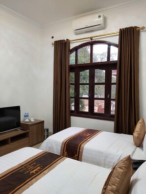 A hotel room with two beds, a TV, a small table with water bottles, and an air conditioning unit. - Van Xuan Royal Hotel (Hoa Lu)