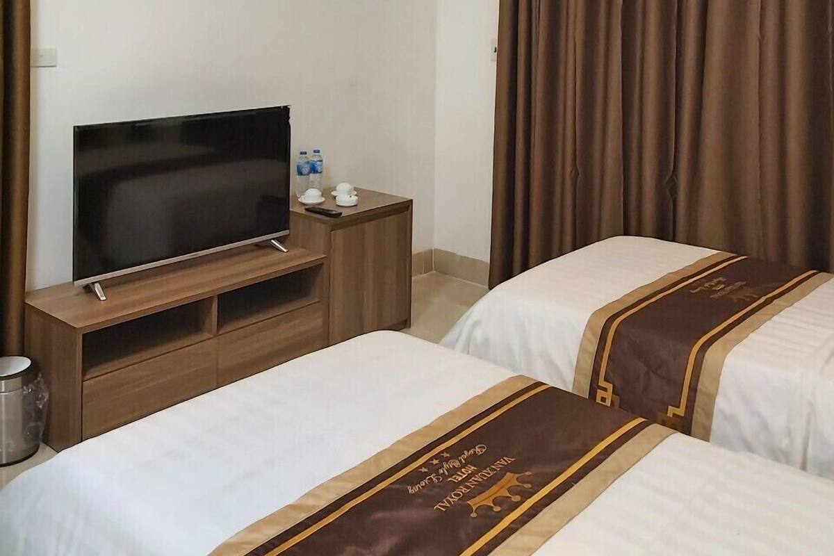 A hotel room with two beds, a TV on a wooden stand, and an air conditioning unit on the ceiling.