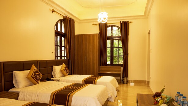 A hotel room with two beds, a wooden headboard, a dining table with plates and bottled water, and a view of greenery through the window. - Van Xuan Royal Hotel (Ninh Binh)