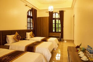 A hotel room with two beds, a wooden headboard, a dining table with plates and bottled water, and a view of greenery through the window. - Van Xuan Royal Hotel (Hoa Lu)